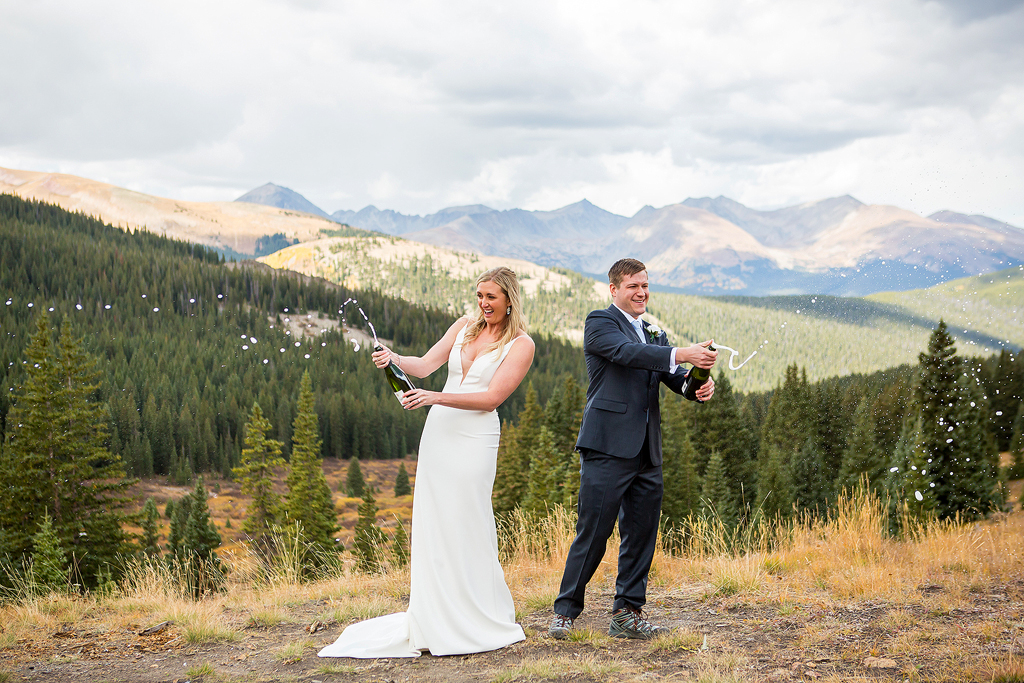 Couple shaking champagne bottles on their wedding day in front of a mountain landscape in Colorado.