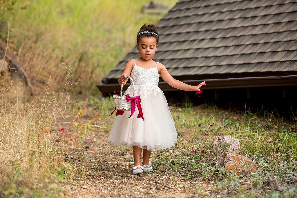 Flower girl walks down the aisle dropping red flower petals.