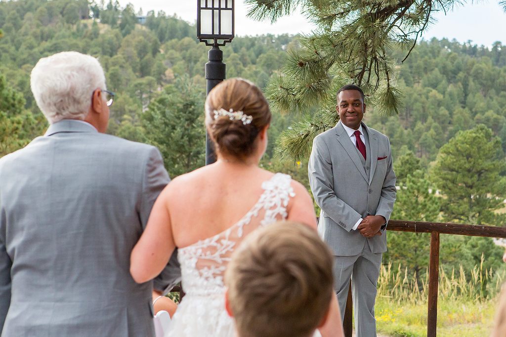 Groom smiles behind the bride walking with her dad.