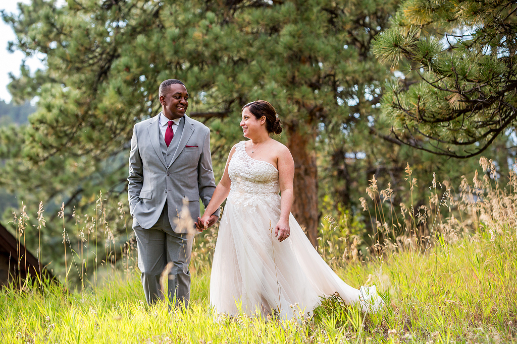 Bride and groom walk through a grassy meadow in a Colorado pine forest.