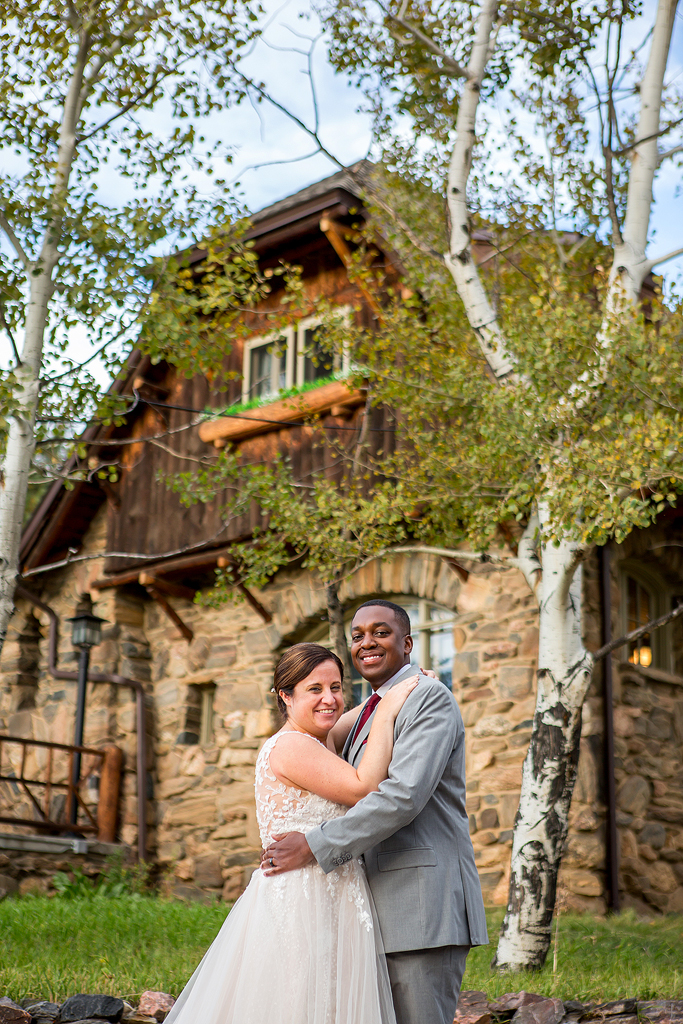 The stone and wood Chief Hosa Lodge stands tall behind the bride and groom as they hug and look at the camera.