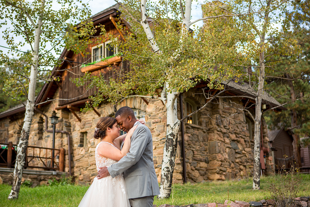 Bride and groom snuggle surrounded by aspen trees and the Lodge behind them.