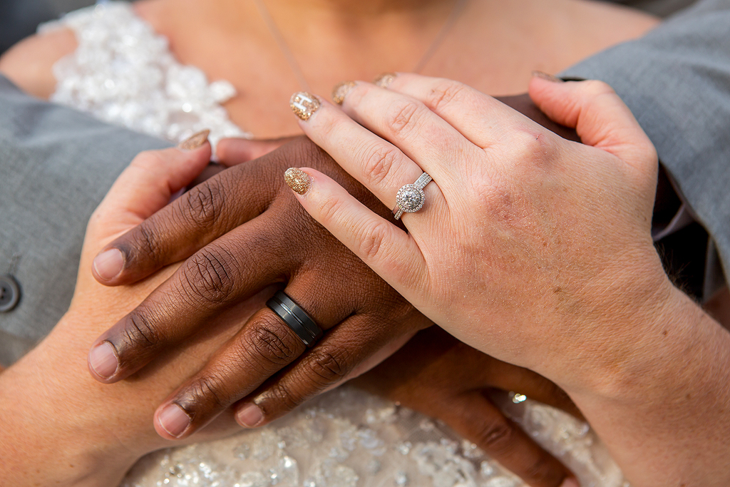 Close-up of wedding rings and bride and groom hands clasped together.