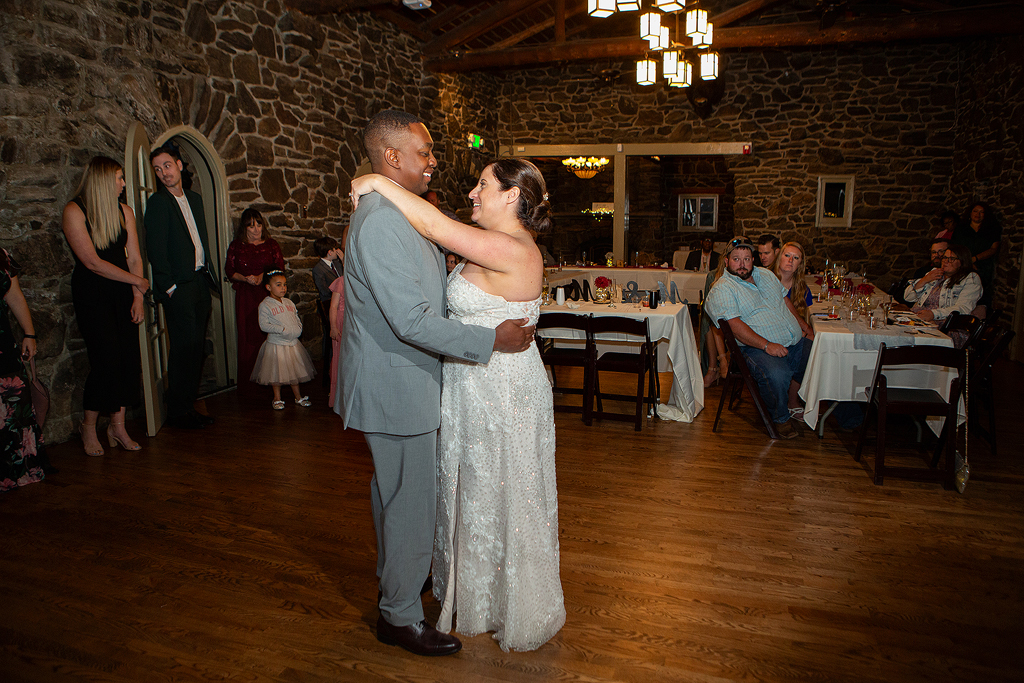 Bride and groom dance with guests behind them in a stone lodge near Evergreen, CO.