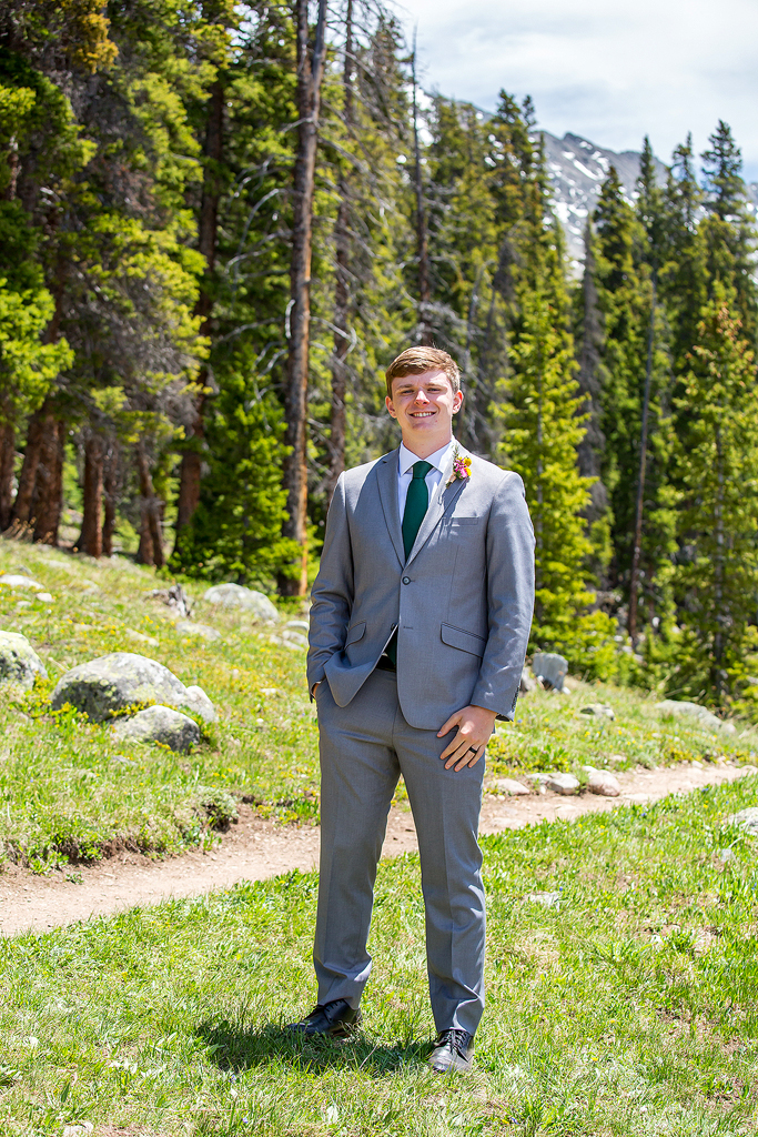 groom portrait in front of pine trees and a trail.
