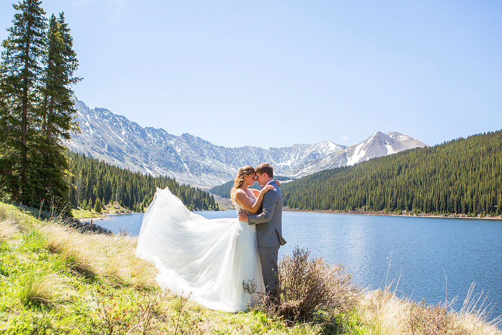 Madi's wedding dress train blows in the wind with the mountains behind them.