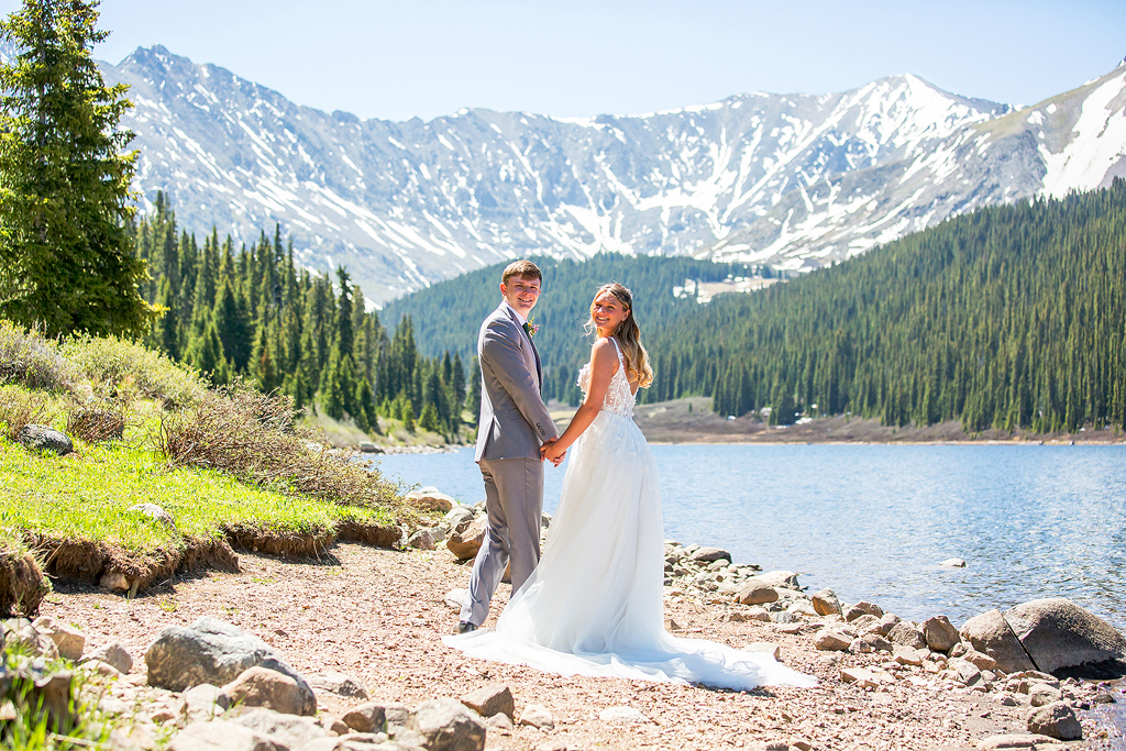Bride and Groom hold hands on the beach of an alpine lake during their mountain elopement.