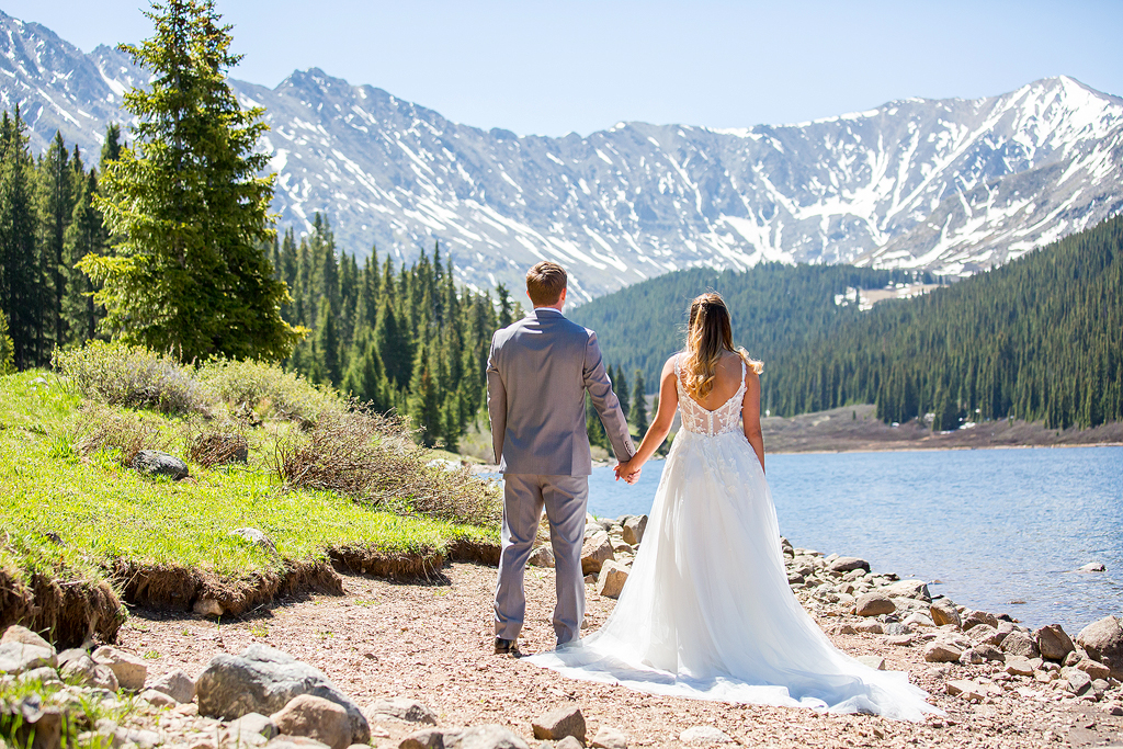 bride and groom take in the mountain view at an alpine lake in Colorado.