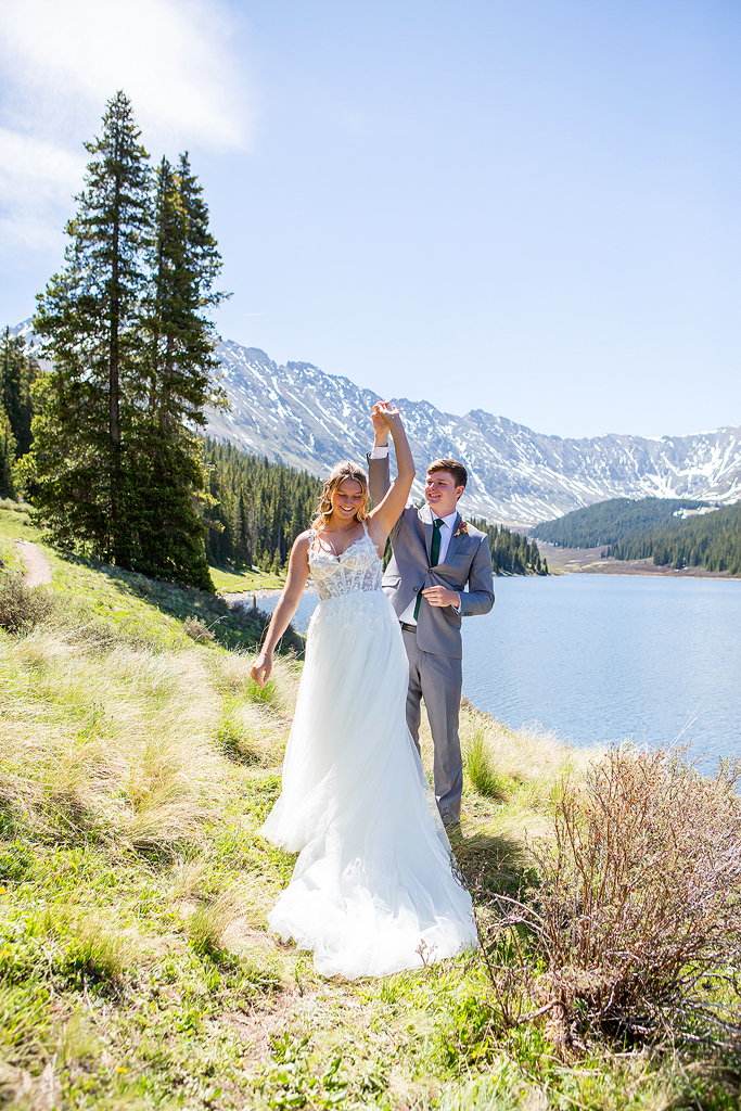 groom twirls bride by an alpine lake with mountain views during their elopement