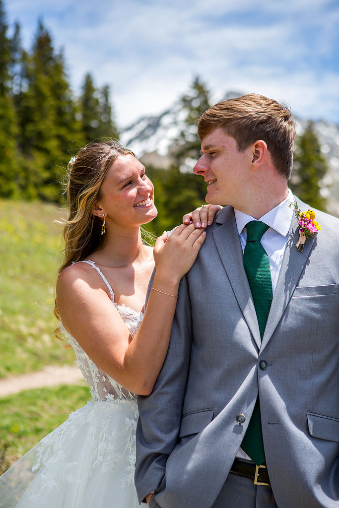 bride hangs on grooms shoulder with pine trees in the background.