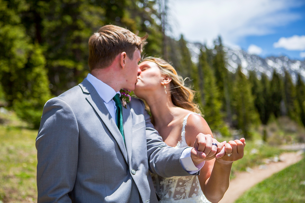 Bride and groom along a mountain trail show off their rings and kiss