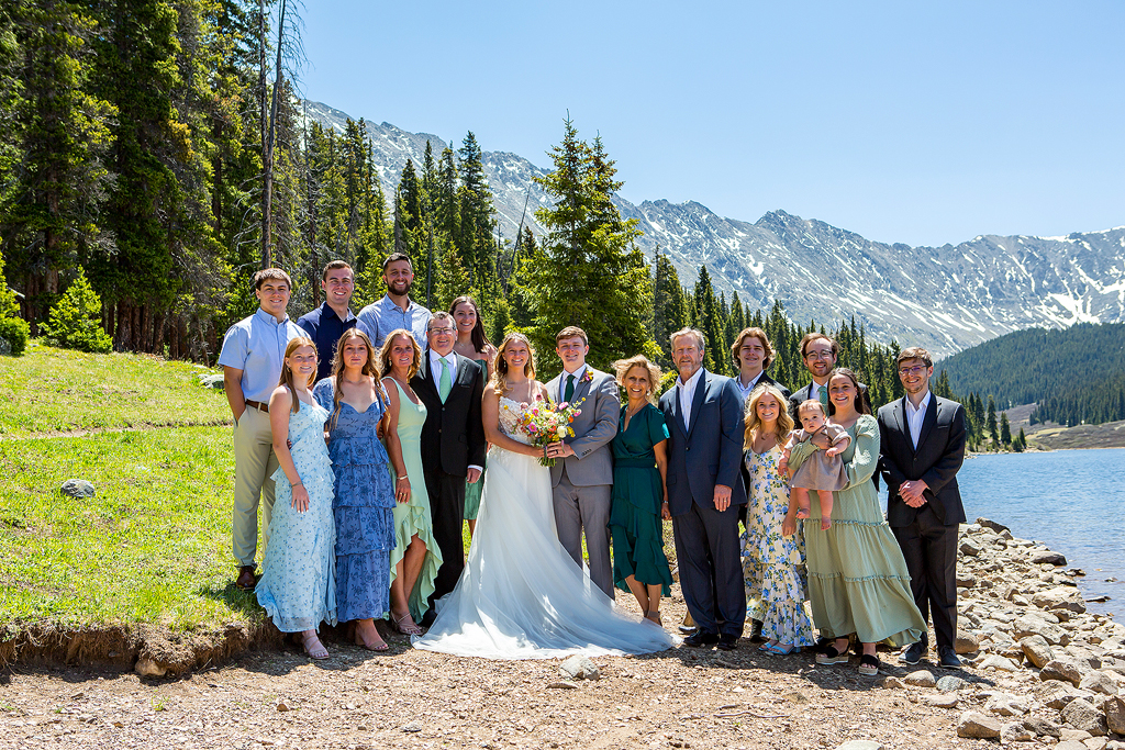 Bride, groom, and all their guests on the beach with mountains behind at Clinton Gulch Dam Reservoir.