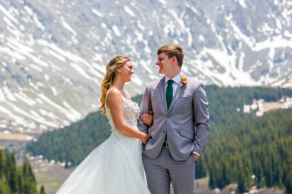 Bridge and groom hug and smile with snow covered mountains in the background.