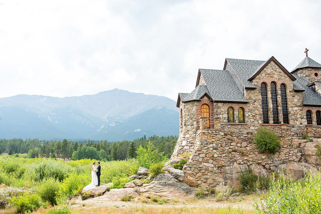 Wedding couple stands at the base of Chapel on the Rock near Estes Park.