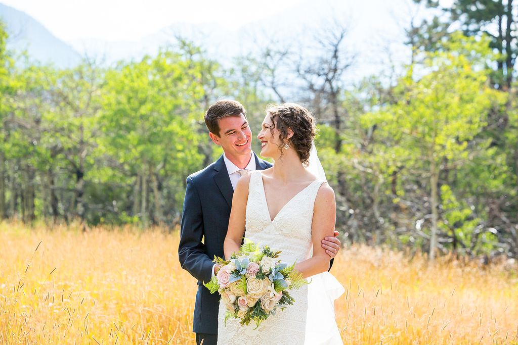 bride and groom smile at each other in a meadow with changing aspens behind them near Estes Park, CO.
