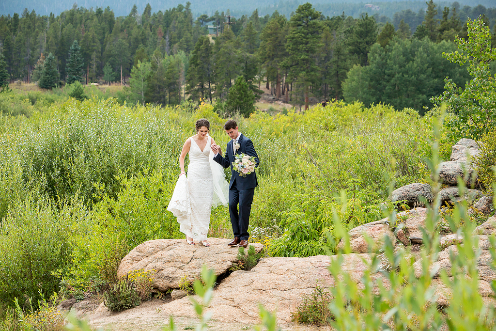 Chip guides Erin by the hand along rocks in front of a pine forest in Allenspark, CO