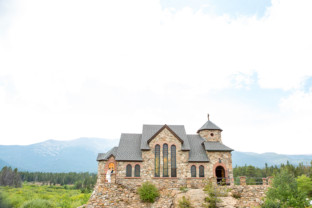 Wide view of Chapel on rock in Colorado with married couple in archway and mountains behind