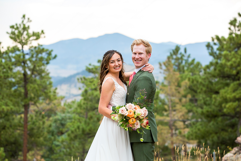 Bride puts her arm around the groom's shoulder in front of a mountain view and pine trees in Golden Colorado.