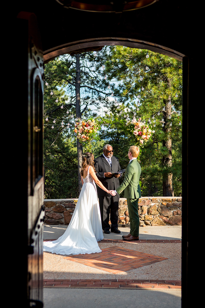 Bride and groom hold hands during their Boettcher Mansion wedding ceremony framed by an old wood door frame.