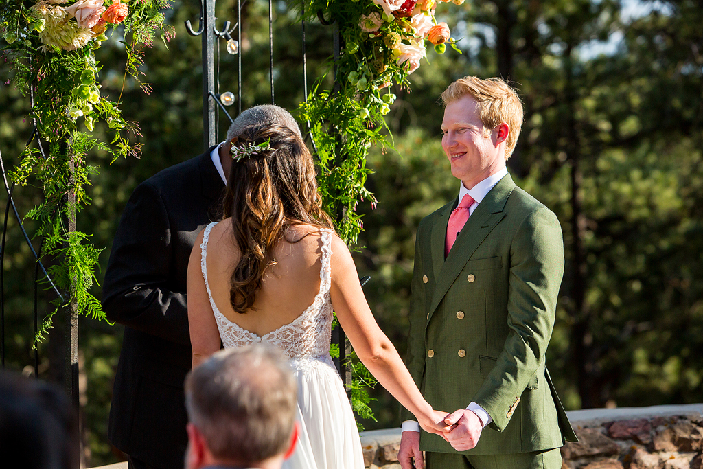 Groom smiles in front of a pine forest during wedding ceremony in Golden, CO