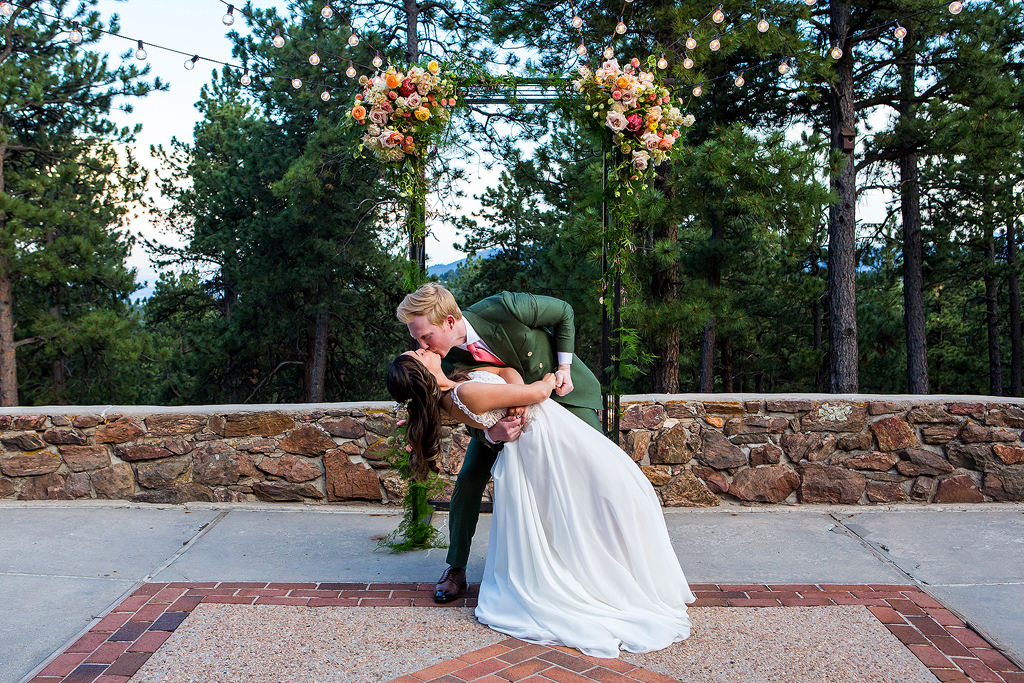Groom dip.s bride in front of their ceremony arch at Boettcher Mansion