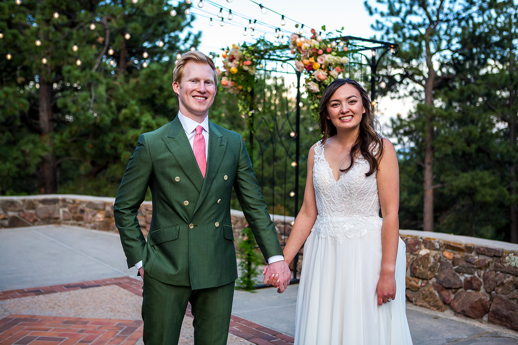 Bride and groom hold hands in front of their ceremony arch with lights.
