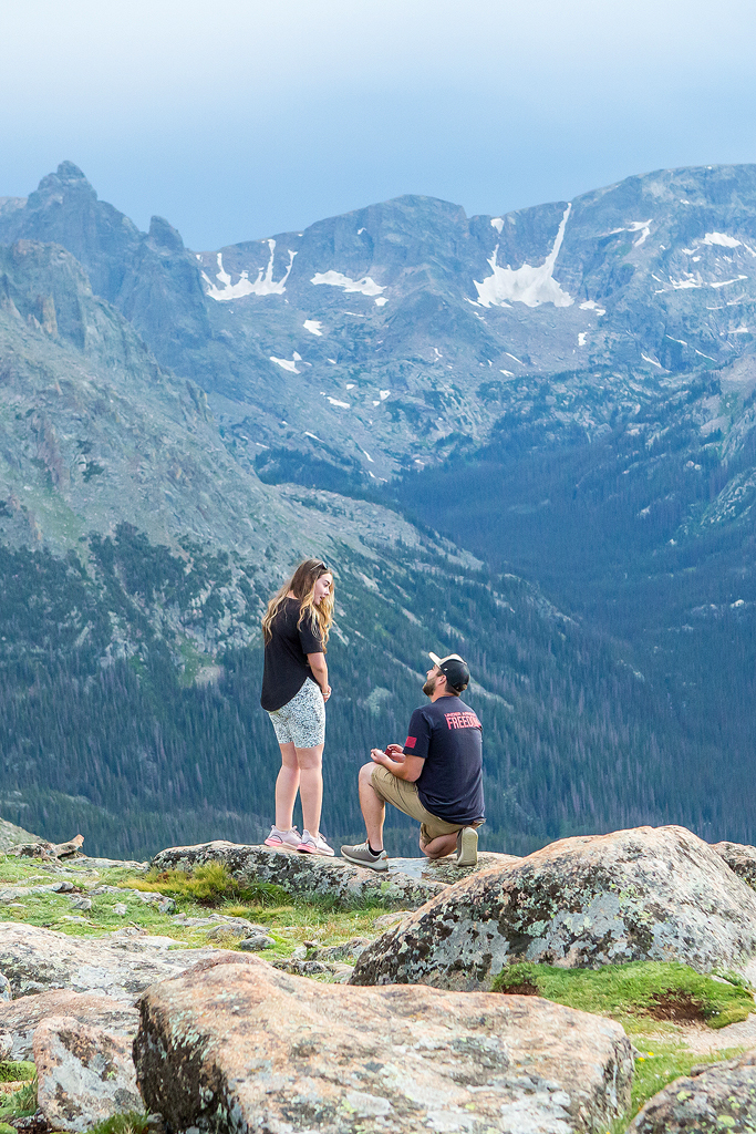Zach kneels in front of large mountain peaks in Rocky Mountain National Park.