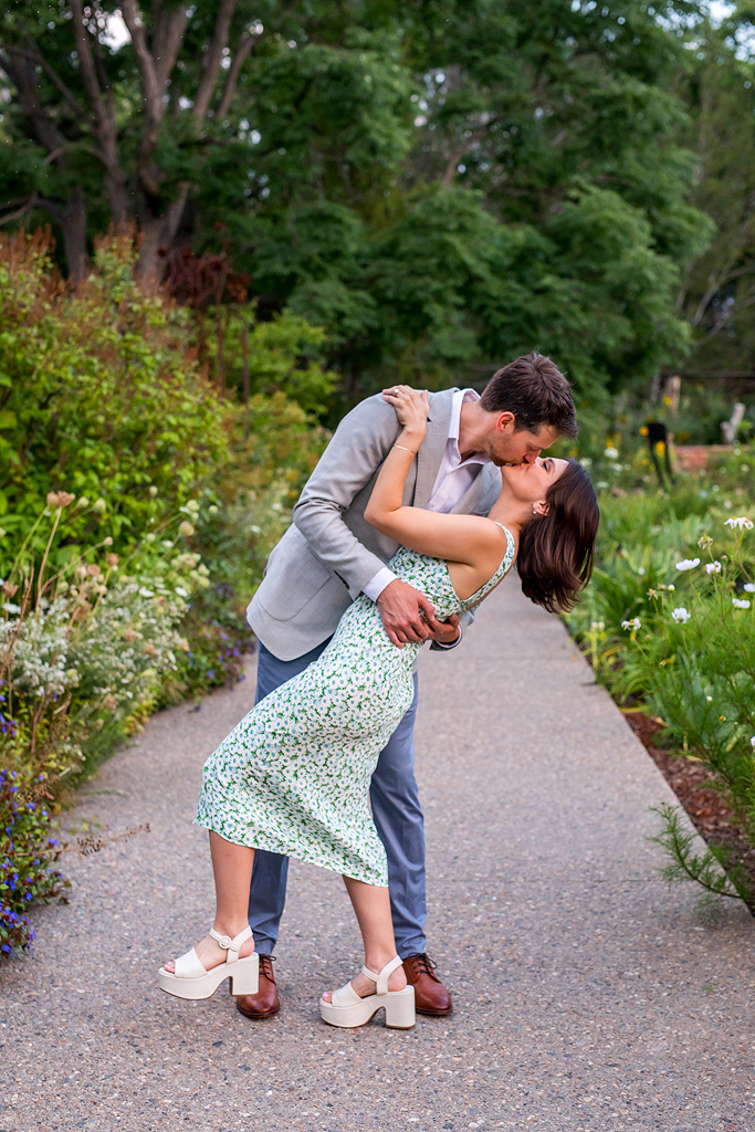 Conor dips Sisana and kisses her on a path at Denver Botanic Gardens surrounded by greenery and trees.