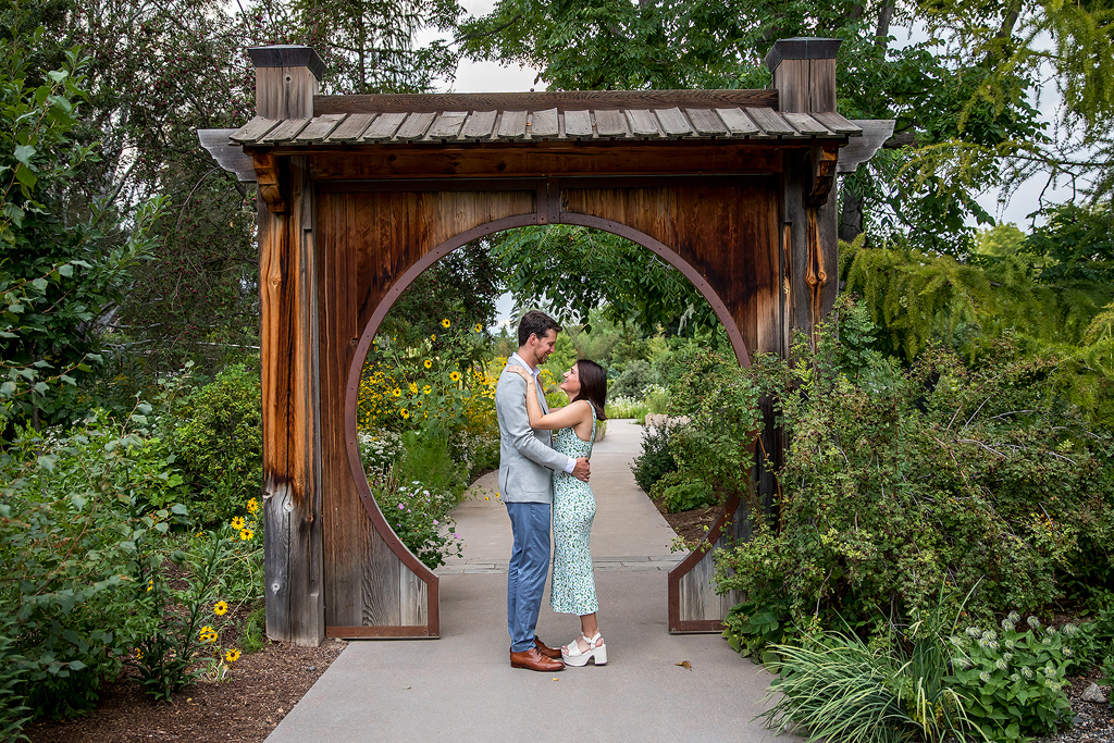 Couple embraces at Denver Botanic Gardens, framed by a wooden arch.