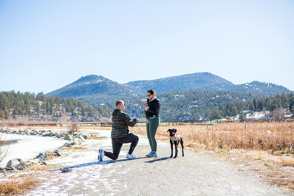 Ryan kneels to propose to Alyssa at Evergreen Lake with their dog.