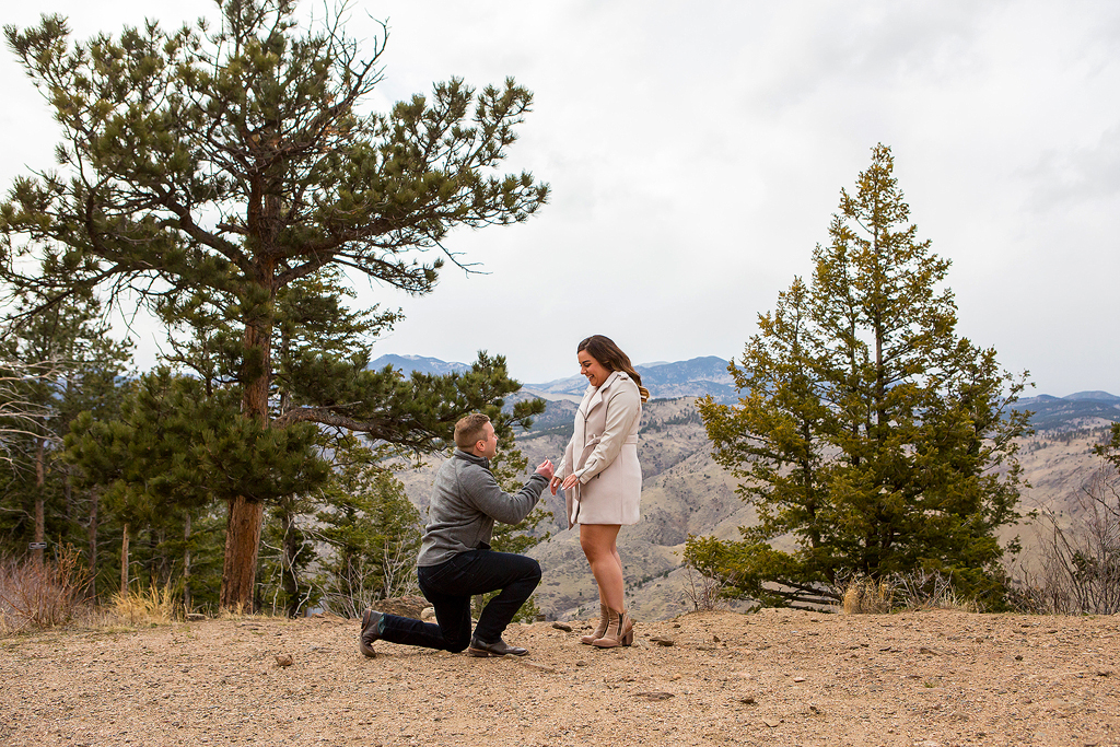 Garrett kneels and holds an engagement ring for Marissa at Lookout Mountain.