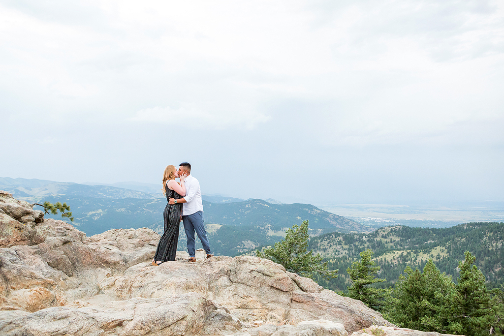 Couple kisses at Lost Gulch Overlook with mountain peaks behind them.