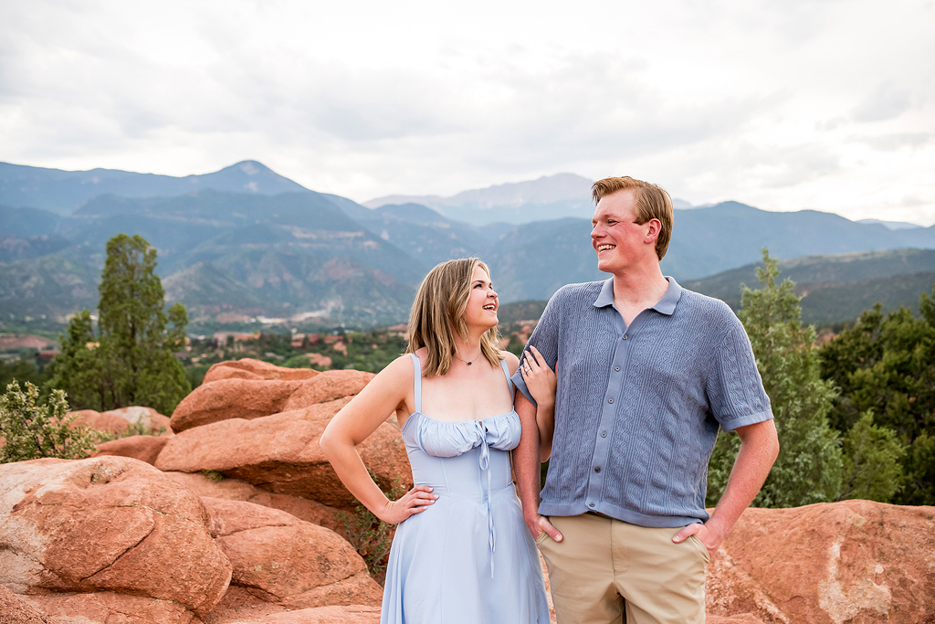 Jenna and Stephen stand on red rocks in front of a mountain view at Garden of the Gods during their Colorado engagement.