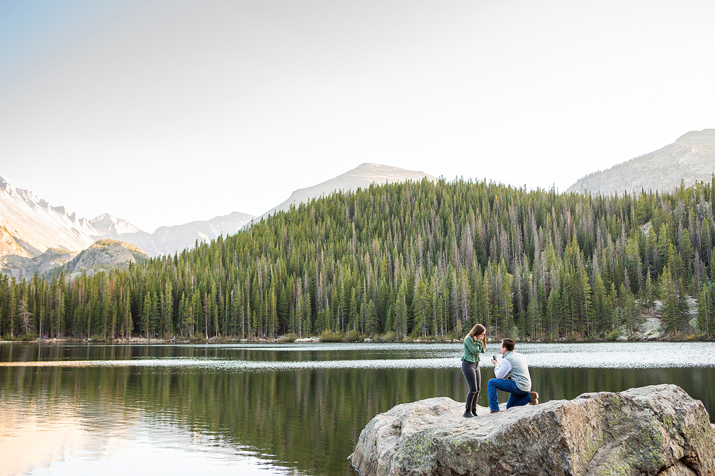 Will kneels on a rock in Bear Lake as he proposes to Erika in Rocky Mountain National Park.