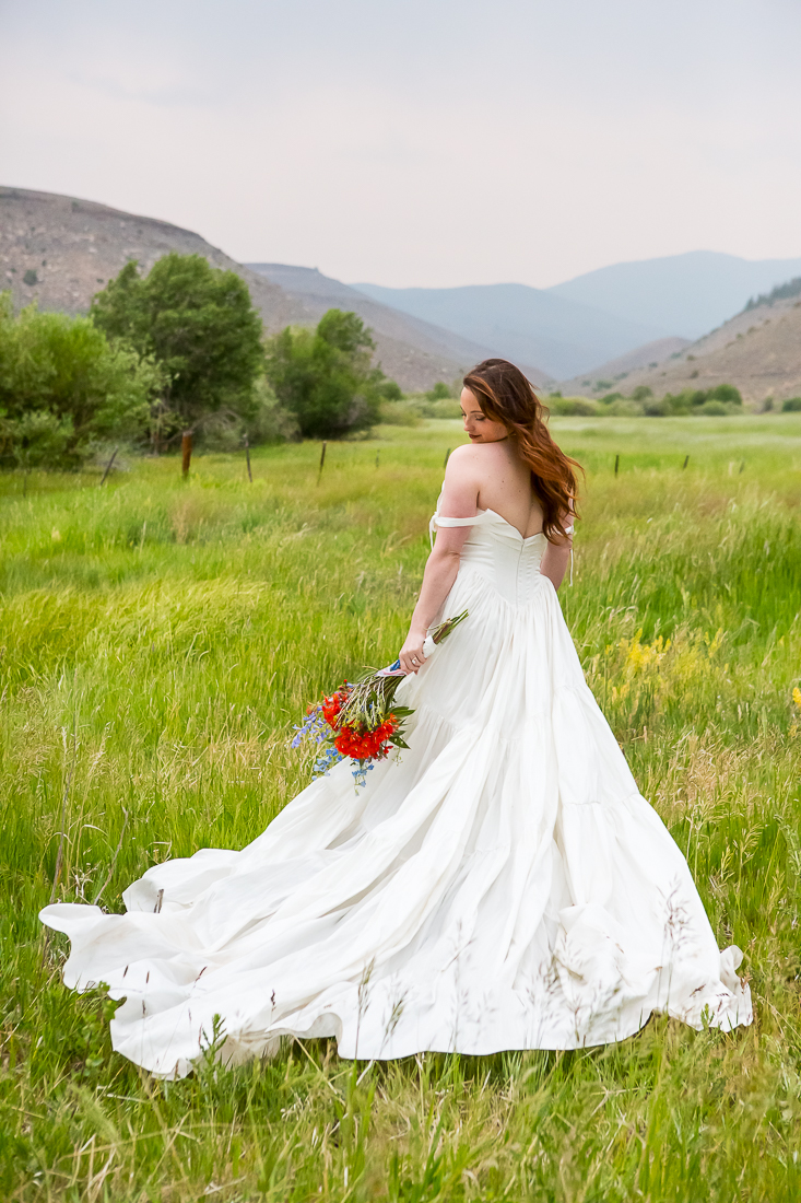 Bride looks down at her flowers wtih her flowy wedding dress fanned out behind her in Colorado.