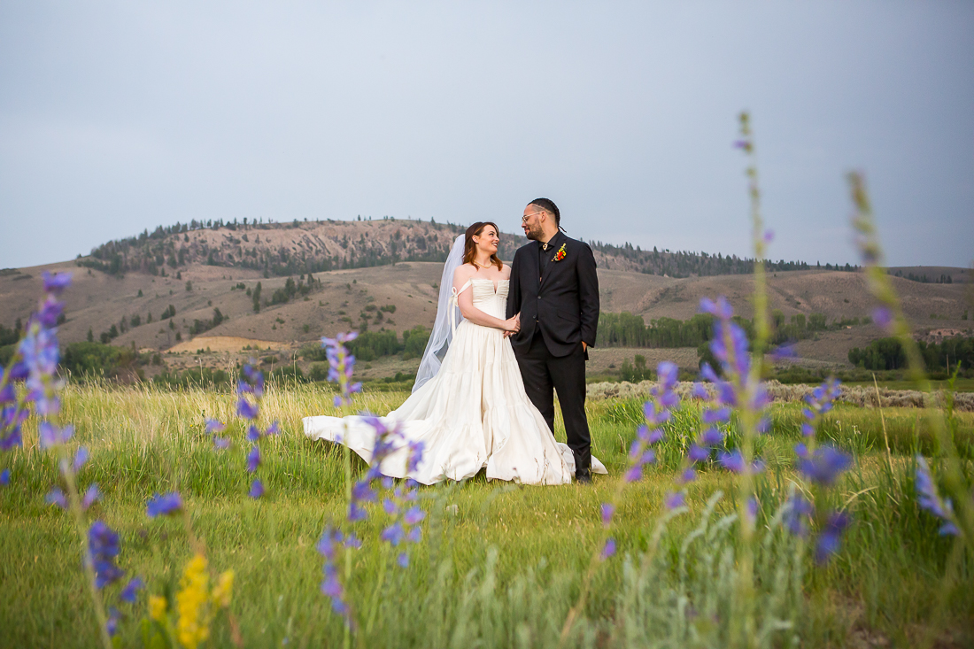 Bride and groom embrace in front of a mountain landscape framed with purple wildflowers during their elopement in Gunnison, Colorado.