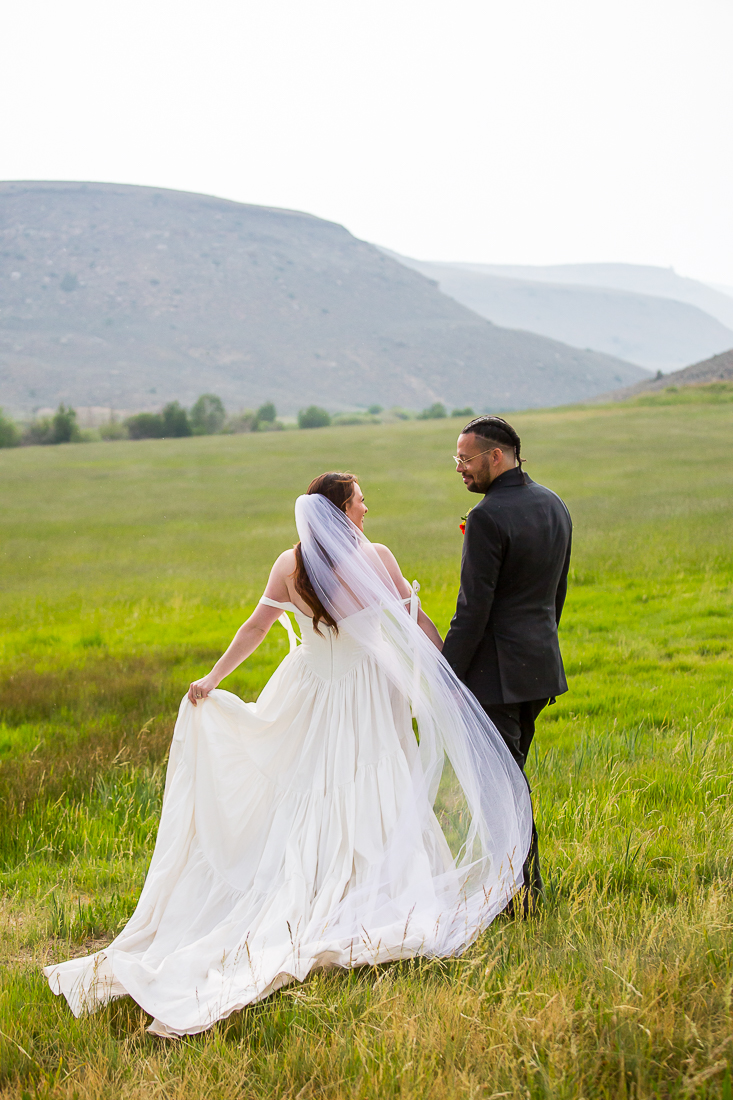 Elopement couple walks through a meadow with the mountains behind them in Gunnison.