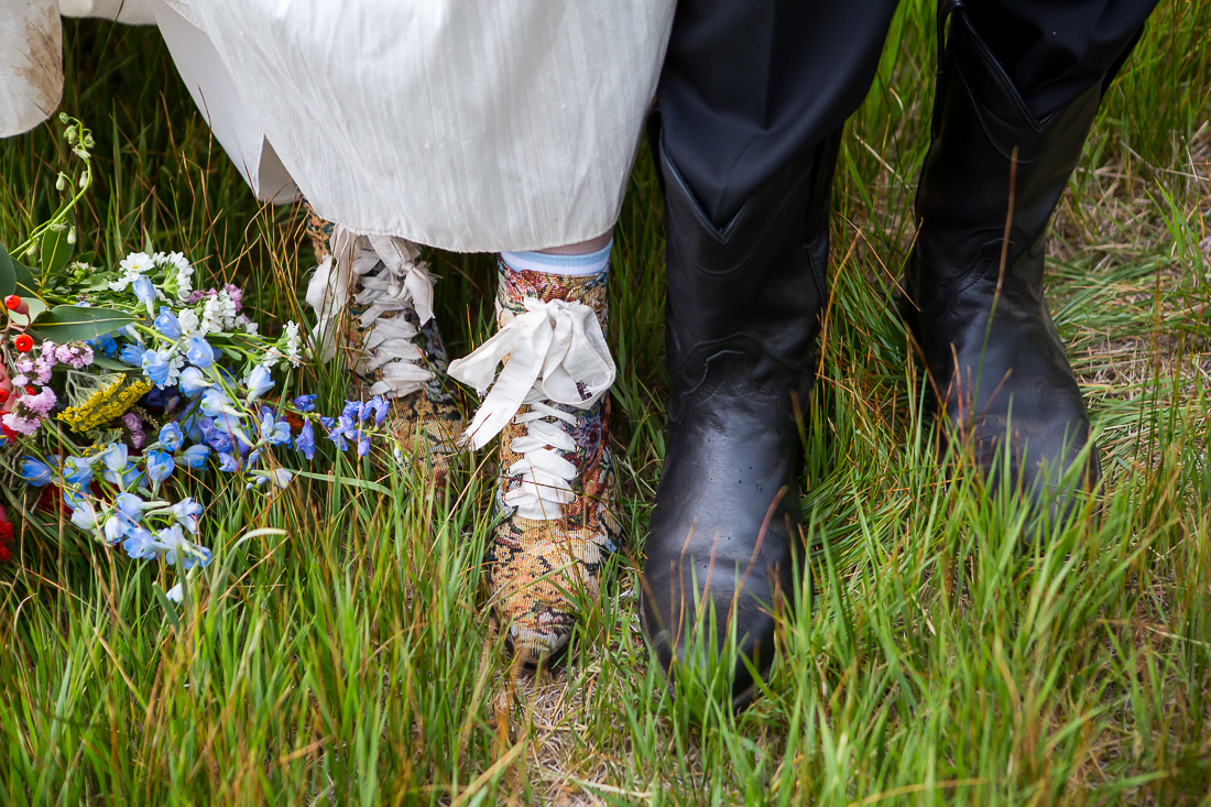 Close up of groom's black boots and bride's vintage boots in the grass in Colorado.